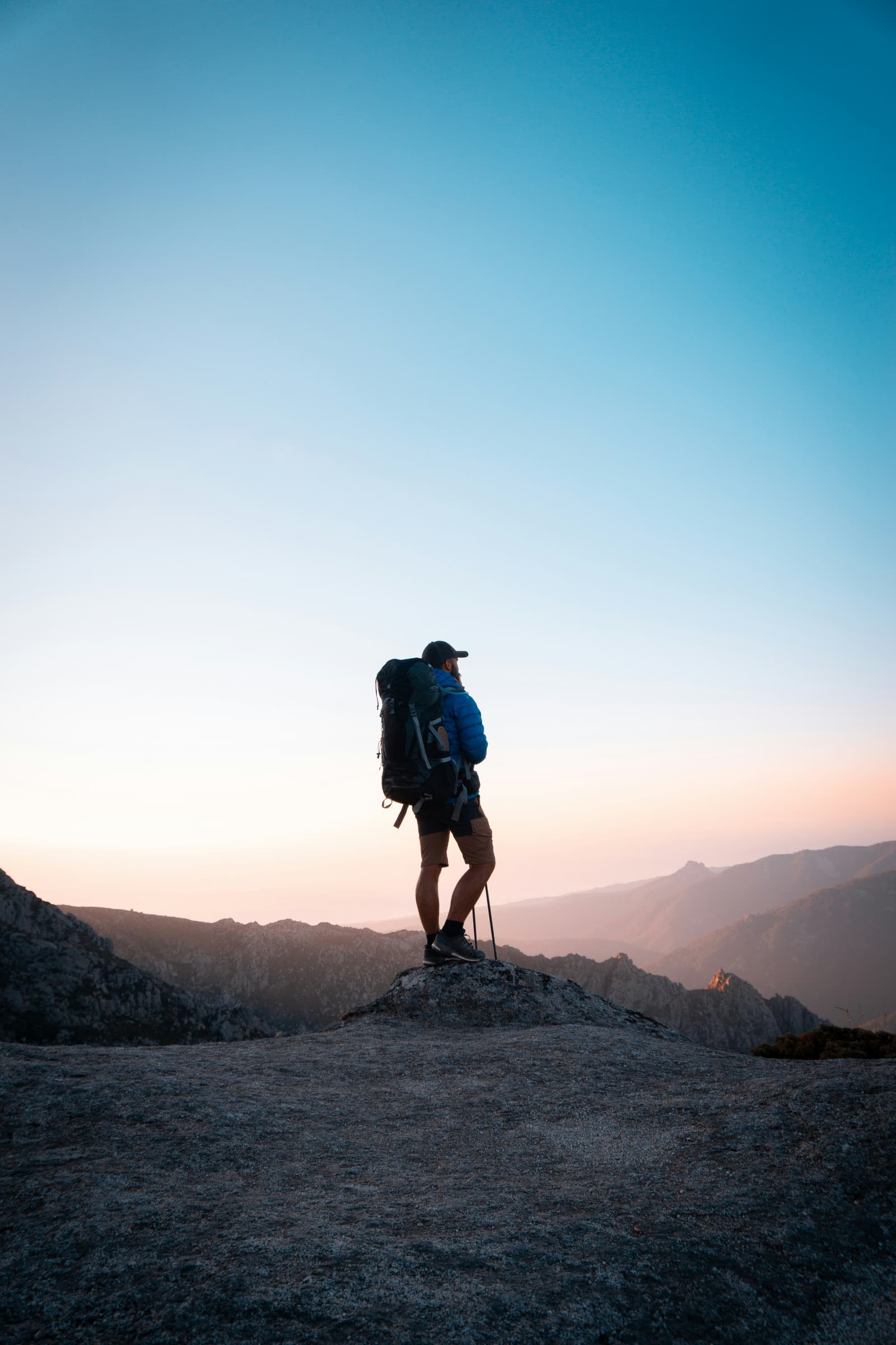 Hiker silhouette with large backpack standing on mountain summit at sunset